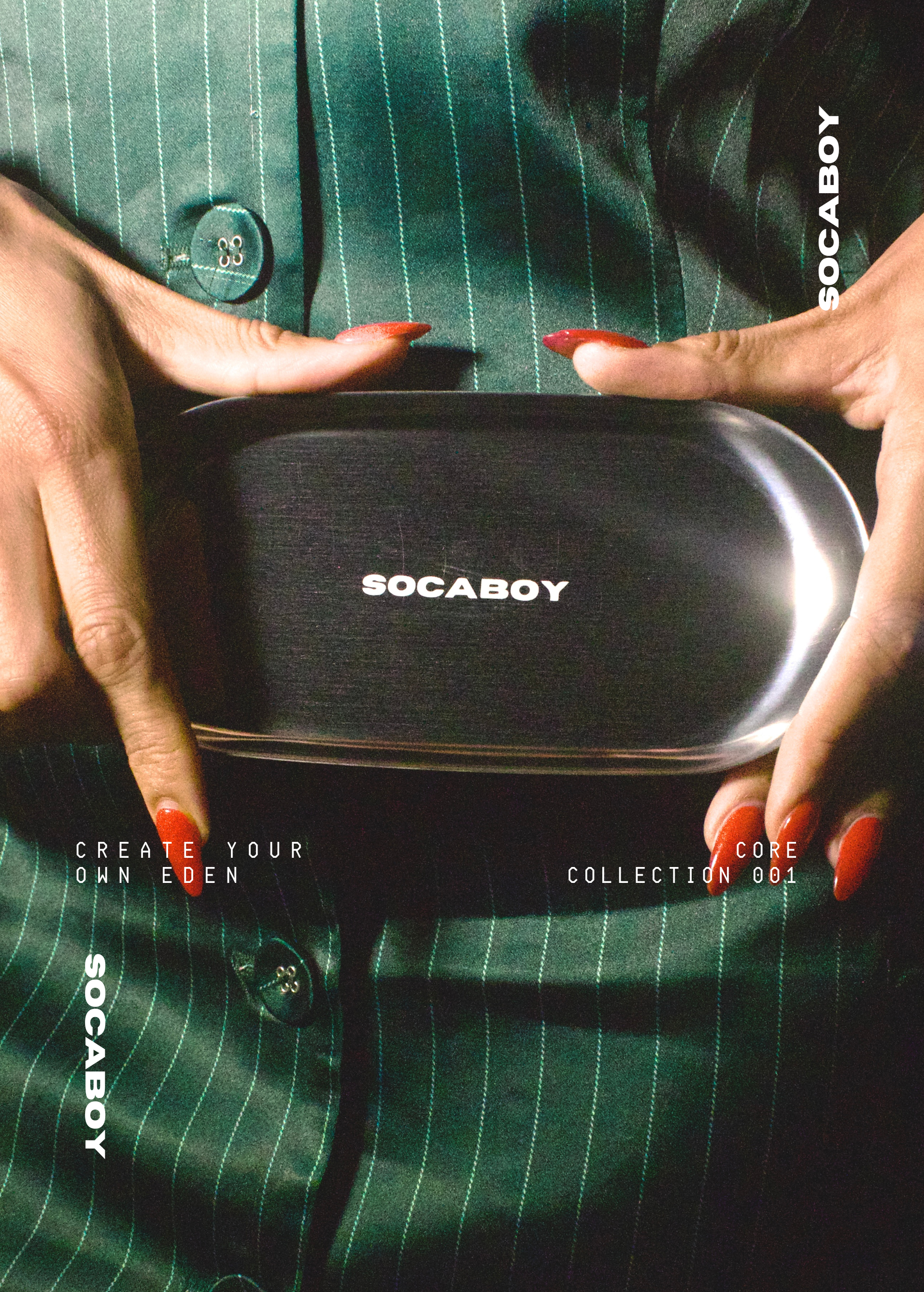 The chrome Socaboy Rolland Tray is held by two hands with bright red long nails. The tray is shining and features the signature logo. The tray is held against a satin green pinstripe jumpsuit.