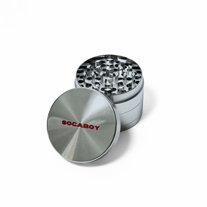 The chrome Socaboy Herb Grinder is photographed against a white backdrop. The lid of the grinder features the logo in red and is resting against the base of the grinder.