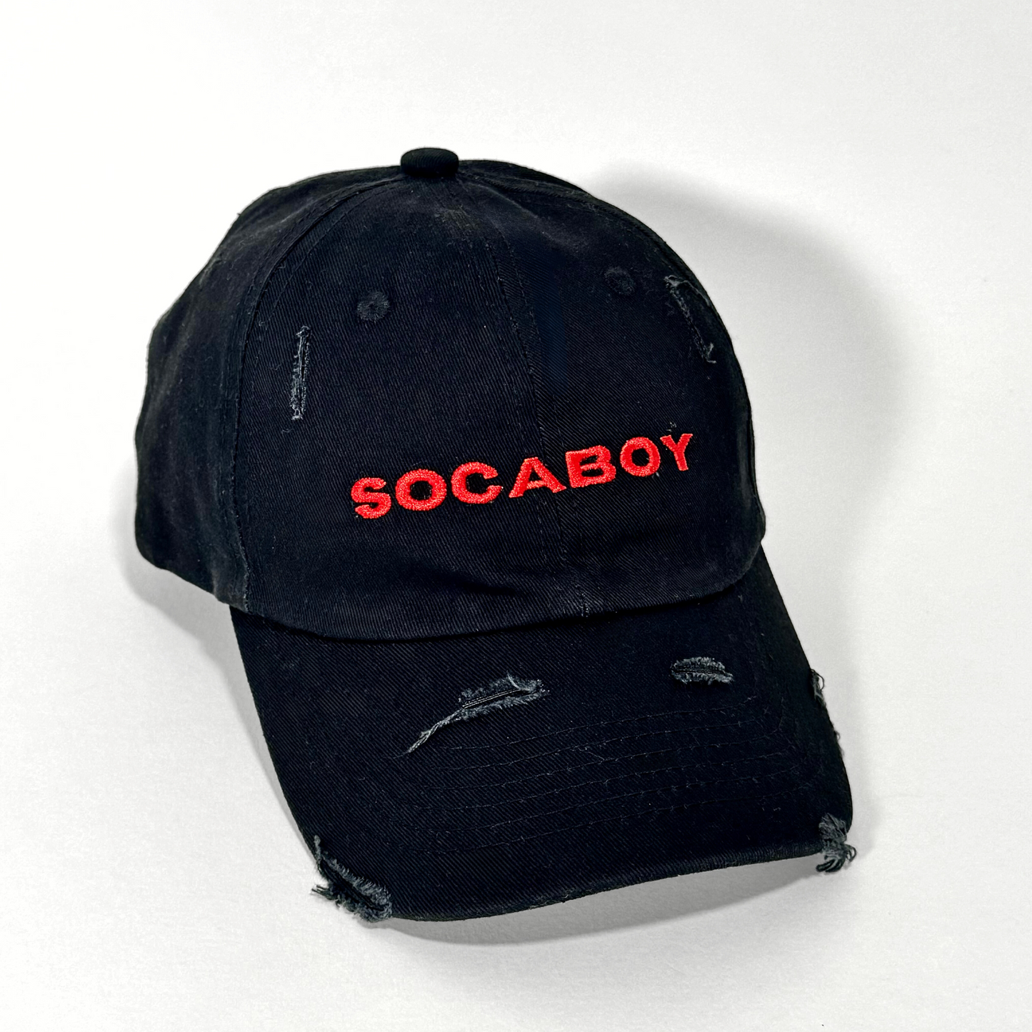 The front of the black Noir Cap is photographed against a white backdrop. The hat features the signature Socaboy logo embroidered in red and has a distressed effect of on the brim and top of the cap.